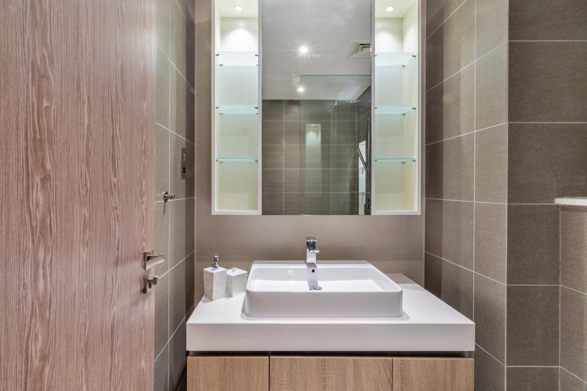A modern bathroom with a white sink, a mirror, and a wooden vanity.