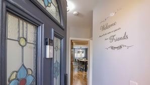 A hallway with a stained glass door, a welcome sign, and a modern kitchen in the background. - Magnolia House (Reading)