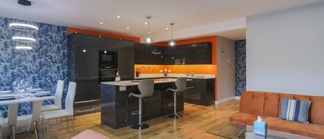A modern kitchen with a central island, bar stools, and a dining area with a glass table and chairs.