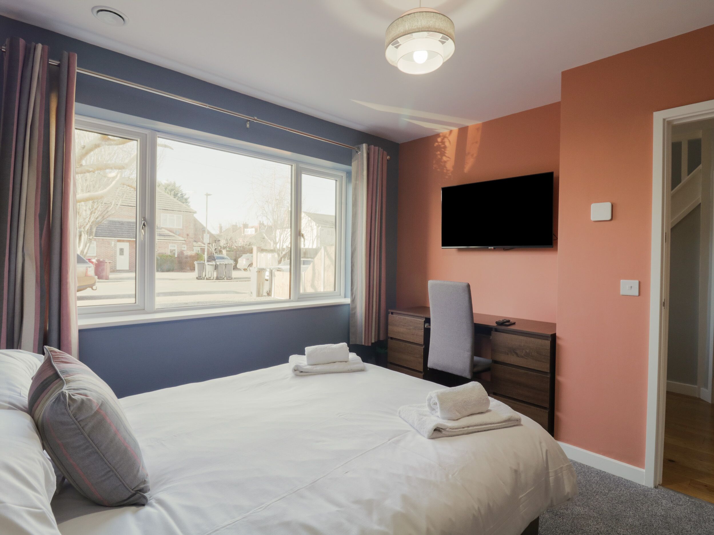 A bedroom with a bed, a desk, a chair, a television, and a window.