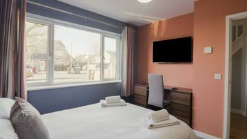 A bedroom with a bed, a desk, a chair, a television, and a window.