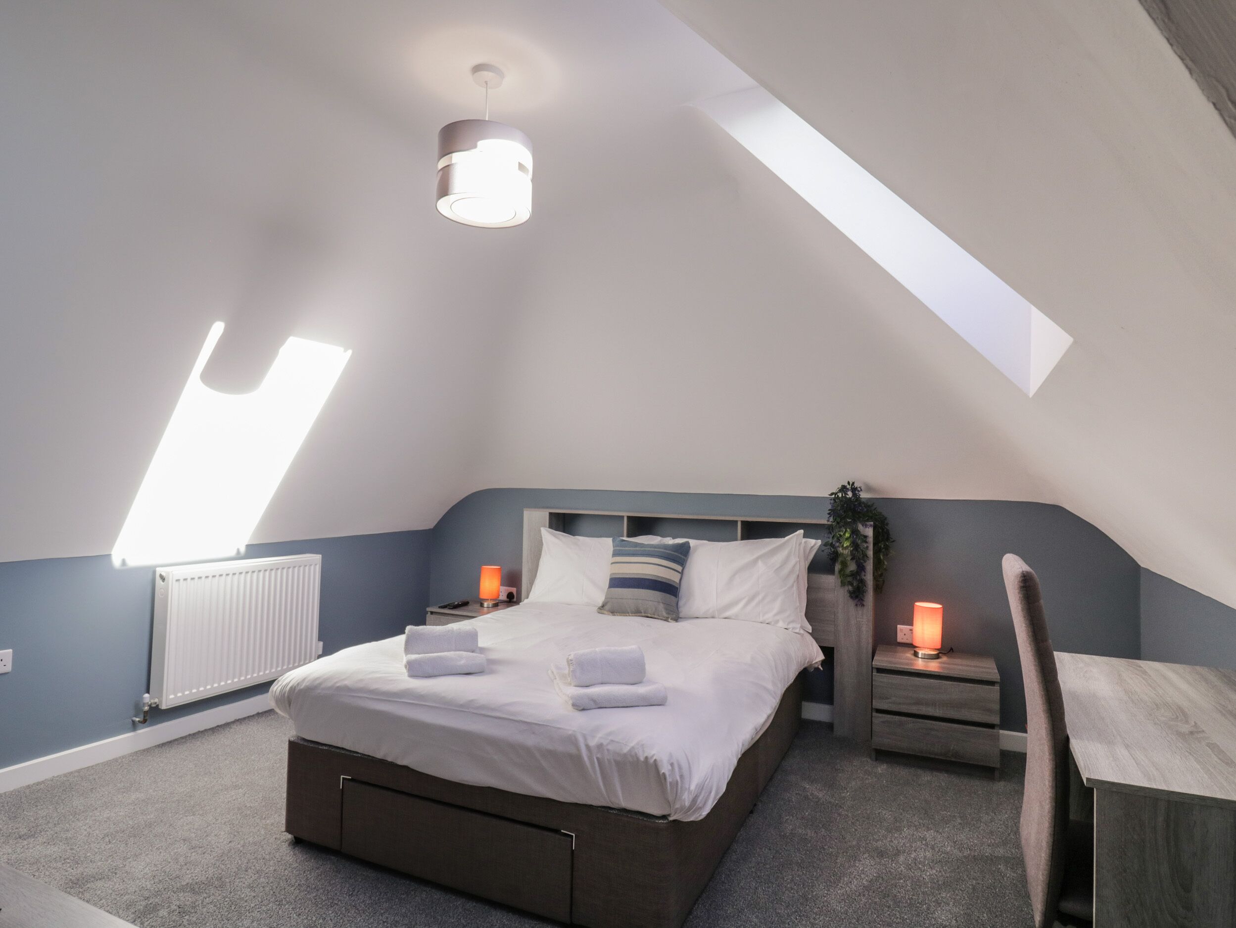 Un dormitorio con cama, mesitas de noche, radiador y tragaluz.