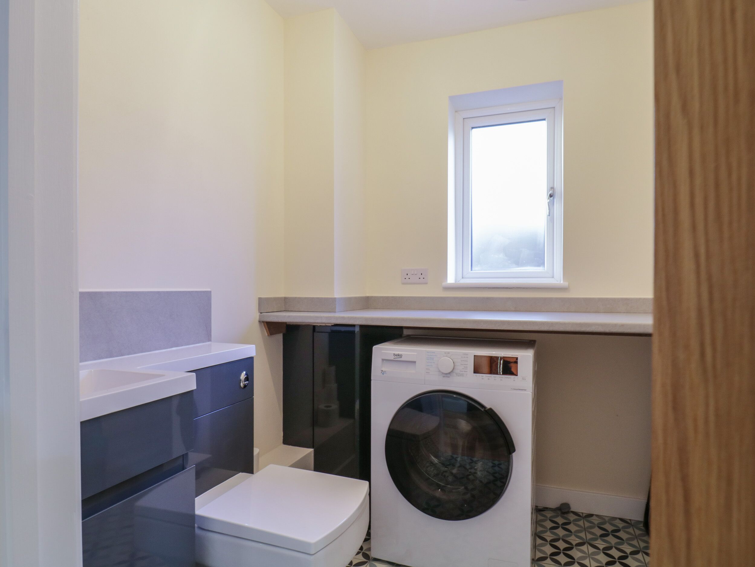 Ein kleiner Hauswirtschaftsraum mit Waschmaschine, Toilette und kleinem Fenster.