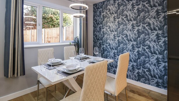A dining area with a white table set for four, a patterned wall, and a window with curtains. - Magnolia House (Reading)