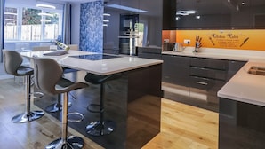 A modern kitchen with a central island, bar stools, and a backsplash with kitchen rules. - Magnolia House (Reading)