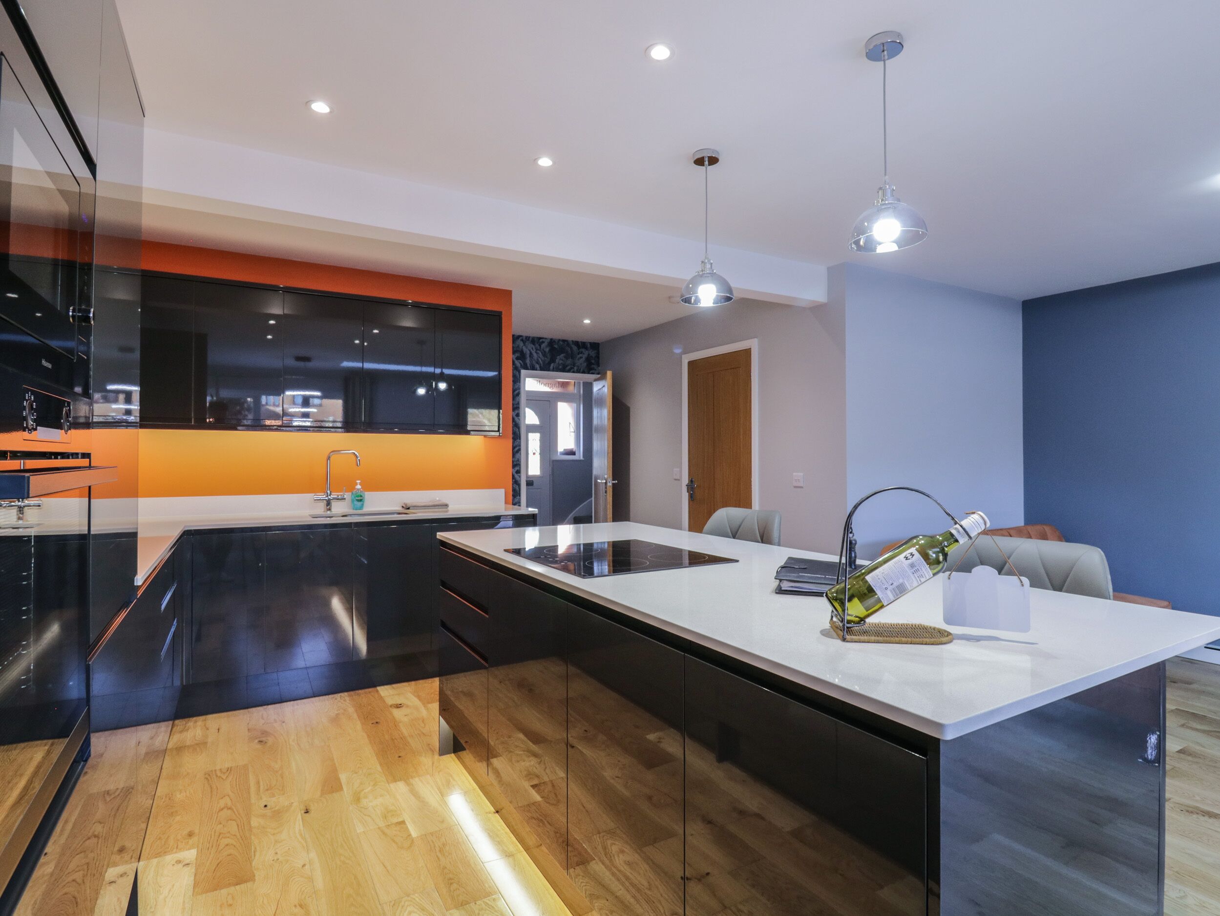 A modern kitchen with a central island, black cabinets, and a wooden floor.