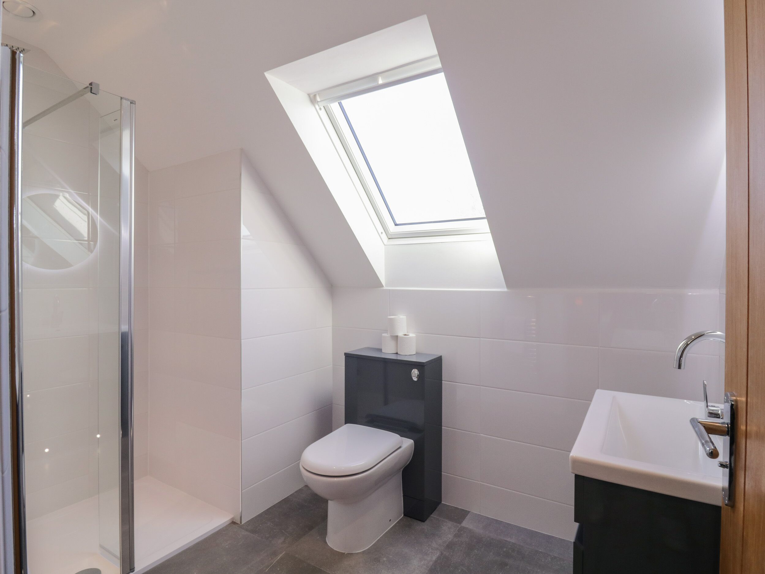 Een moderne badkamer met dakraam, een douchecabine van glas, een toilet en een wastafel.