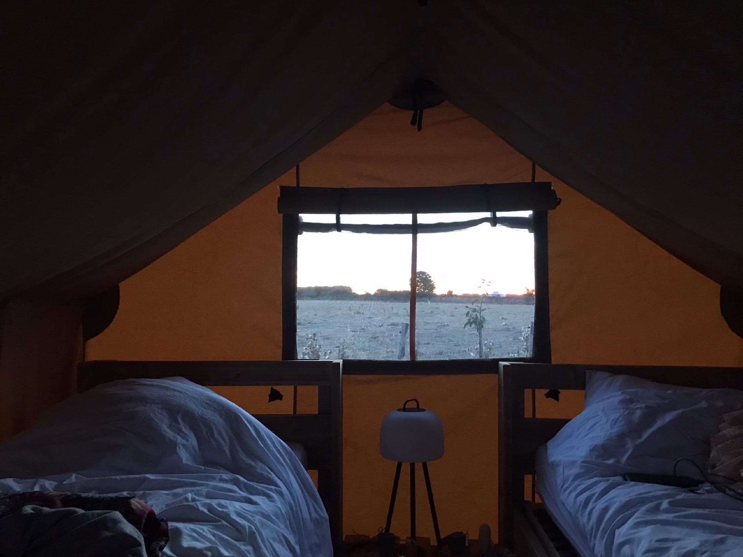 Een knus ingerichte kamer met twee bedden, een raam en een lamp.