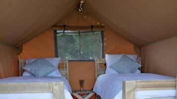 Een tentlodge met twee houten bedden, een raam en een bezem.