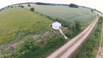 A large, white, cylindrical structure in a rural setting with a dirt road leading to it.