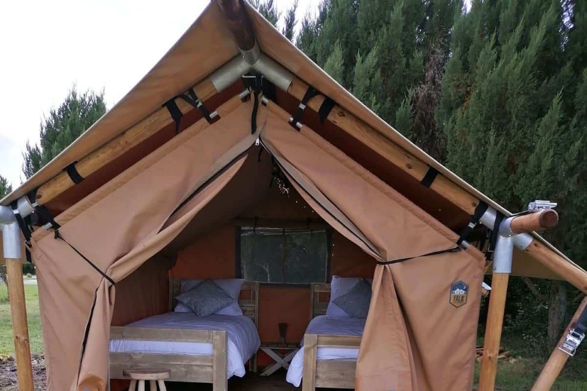 A tent with two beds and a small stool, set on a wooden deck in a forested area.