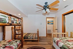 Ein Zimmer mit Etagenbetten, einem Deckenventilator und einer Tür zu einem anderen Raum.