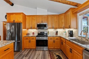 A kitchen with wooden cabinets, stainless steel appliances, granite countertops, and a patterned backsplash.
