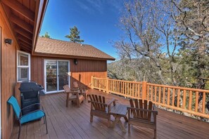 A wooden deck with outdoor furniture, a covered area with a grill, and a view of trees and hills. - Located in the Castle Glen Estates! Recently Remodeled Master! Pet Friendly! Pool Table! Foosball! (Big Bear Lake)