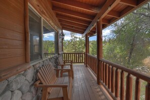 Una terraza de madera con muros de piedra y barandilla, con vista a un área boscosa.