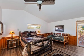 Un dormitorio con una cama grande, dos mesitas de noche, un ventilador de techo, una ventana y una puerta que da a un área exterior.
