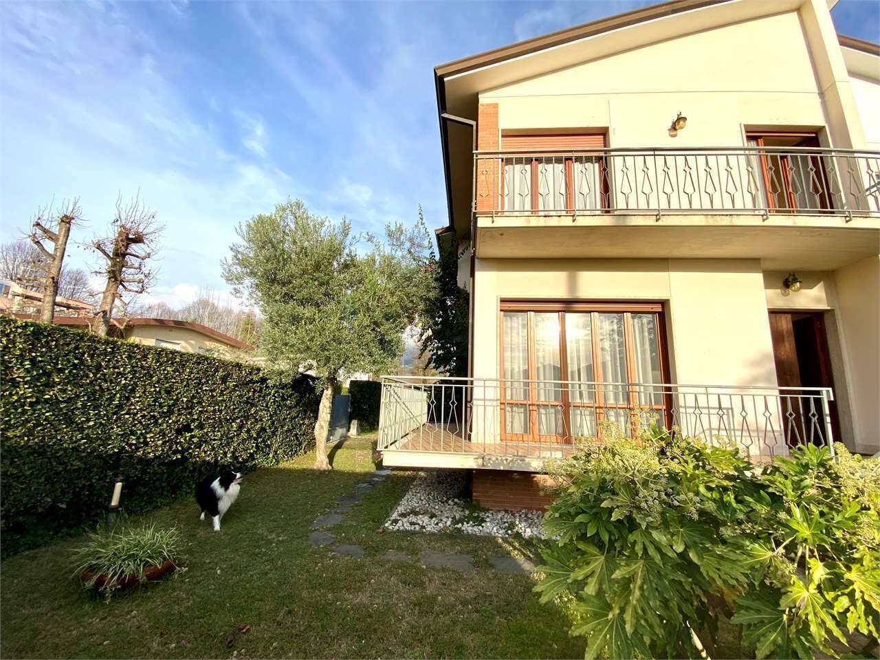 A two-story building with a balcony, a well-maintained garden, and a dog.