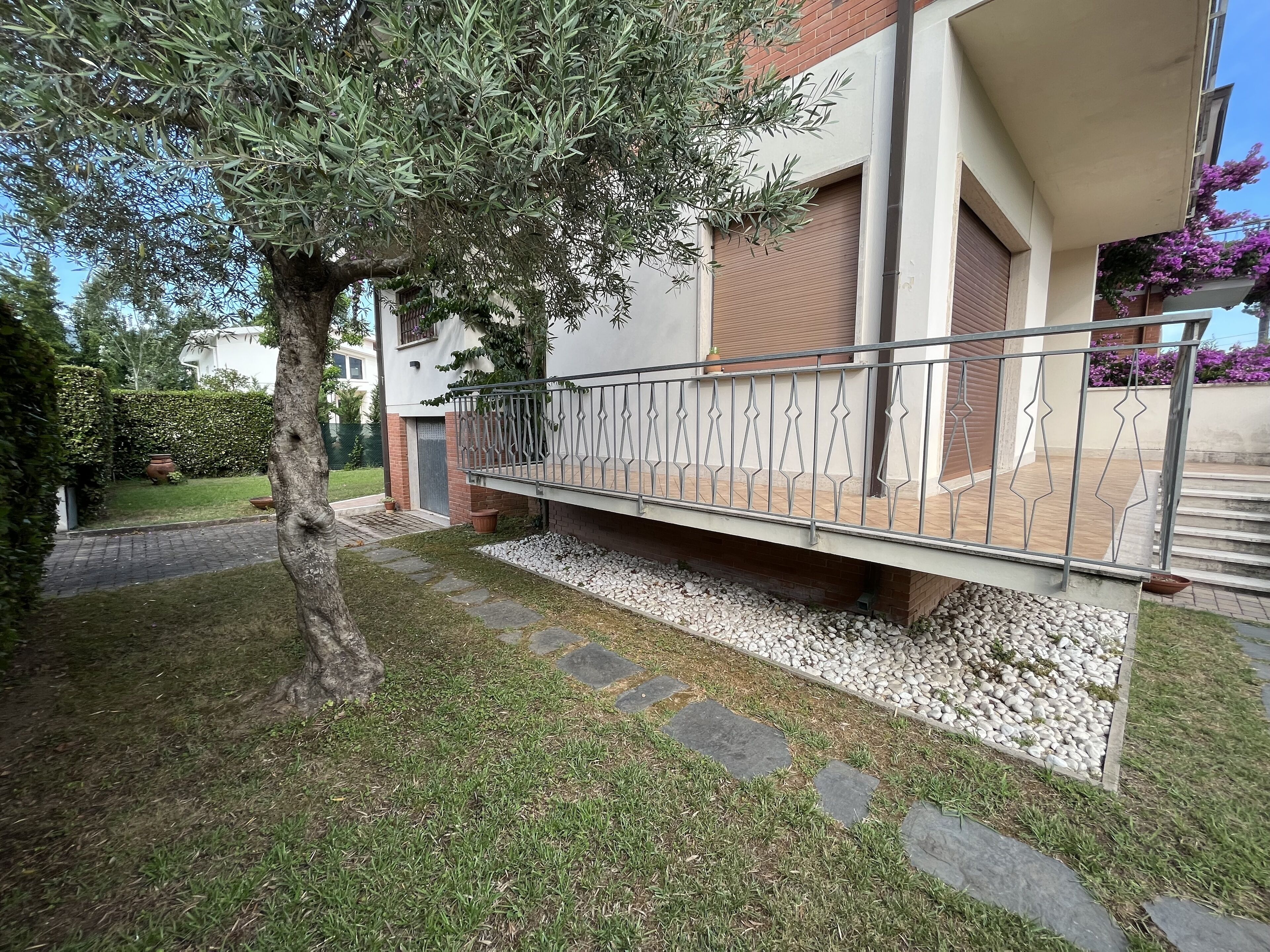 A residential building with a balcony, a tree, and a garden area with stepping stones.