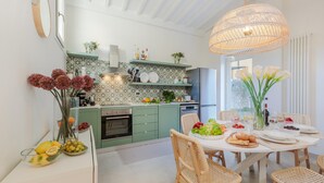 A modern kitchen with green cabinets, a white countertop, and a dining area with wicker chairs and a white table set for a meal. - The City Oasis in Lucca (Lucca)