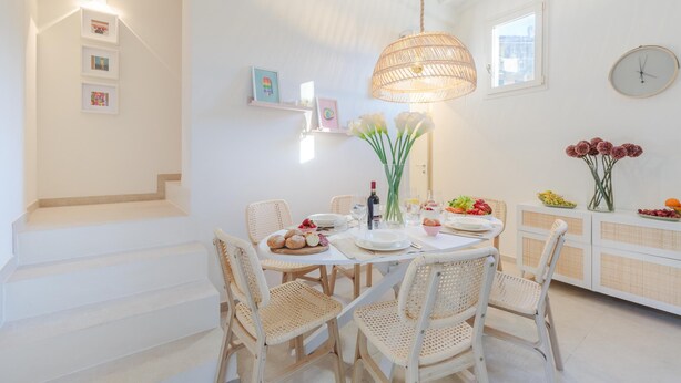 A dining area with a round table, wicker chairs, a hanging light fixture, and a white staircase. - The City Oasis in Lucca (Lucca)