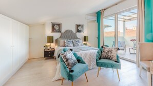 Un dormitorio con cama, dos sillas, una mesita de noche y una ventana con cortinas.