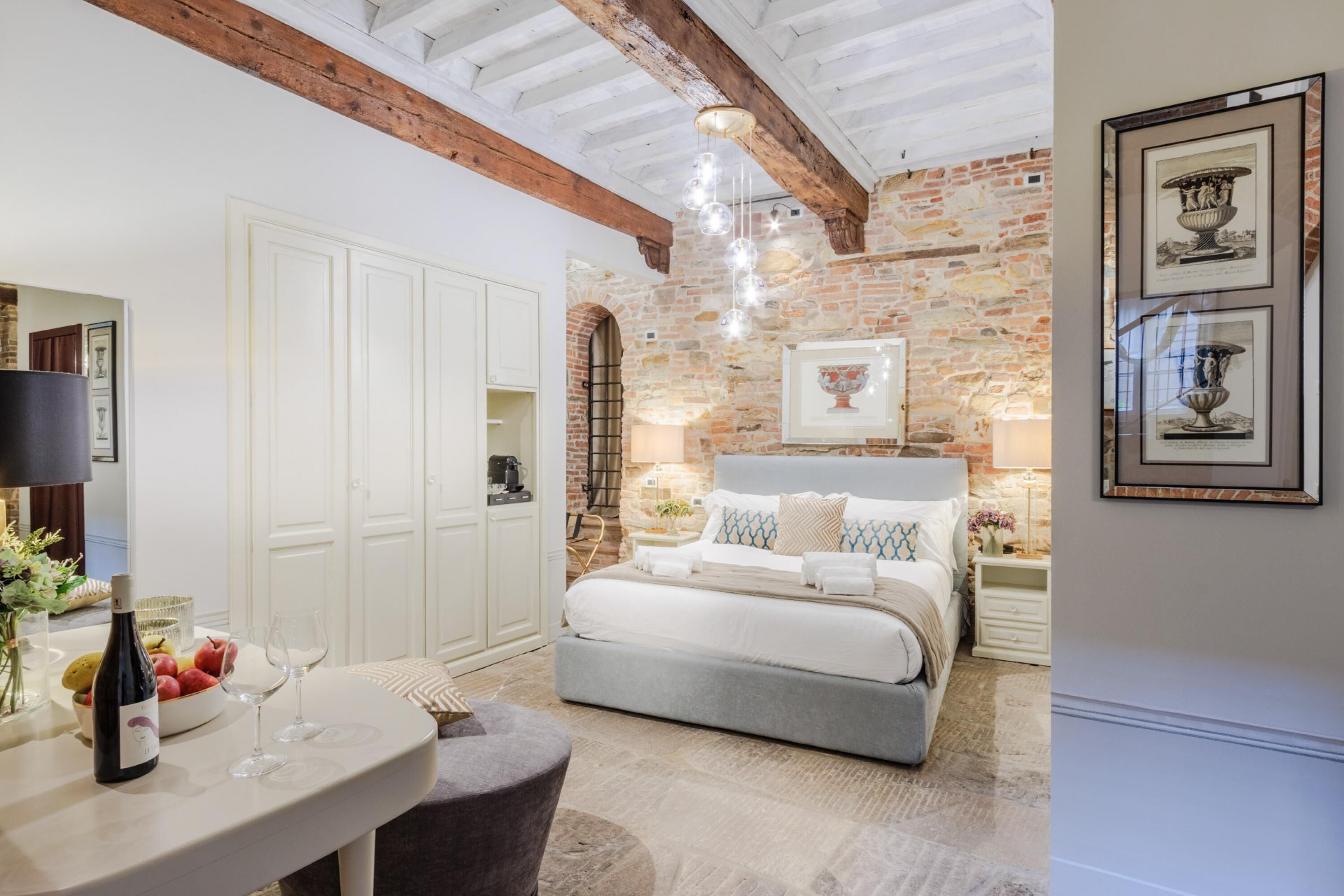 A bedroom with a stone wall, a bed with white bedding, a nightstand with a lamp, and a framed picture on the wall.