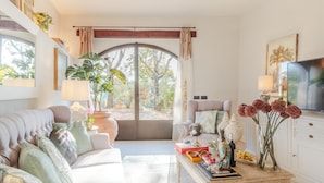 A spacious living room with a large window, a comfortable sofa, a coffee table, and a television. - Amore Farmhouse Retreat (Lucca)