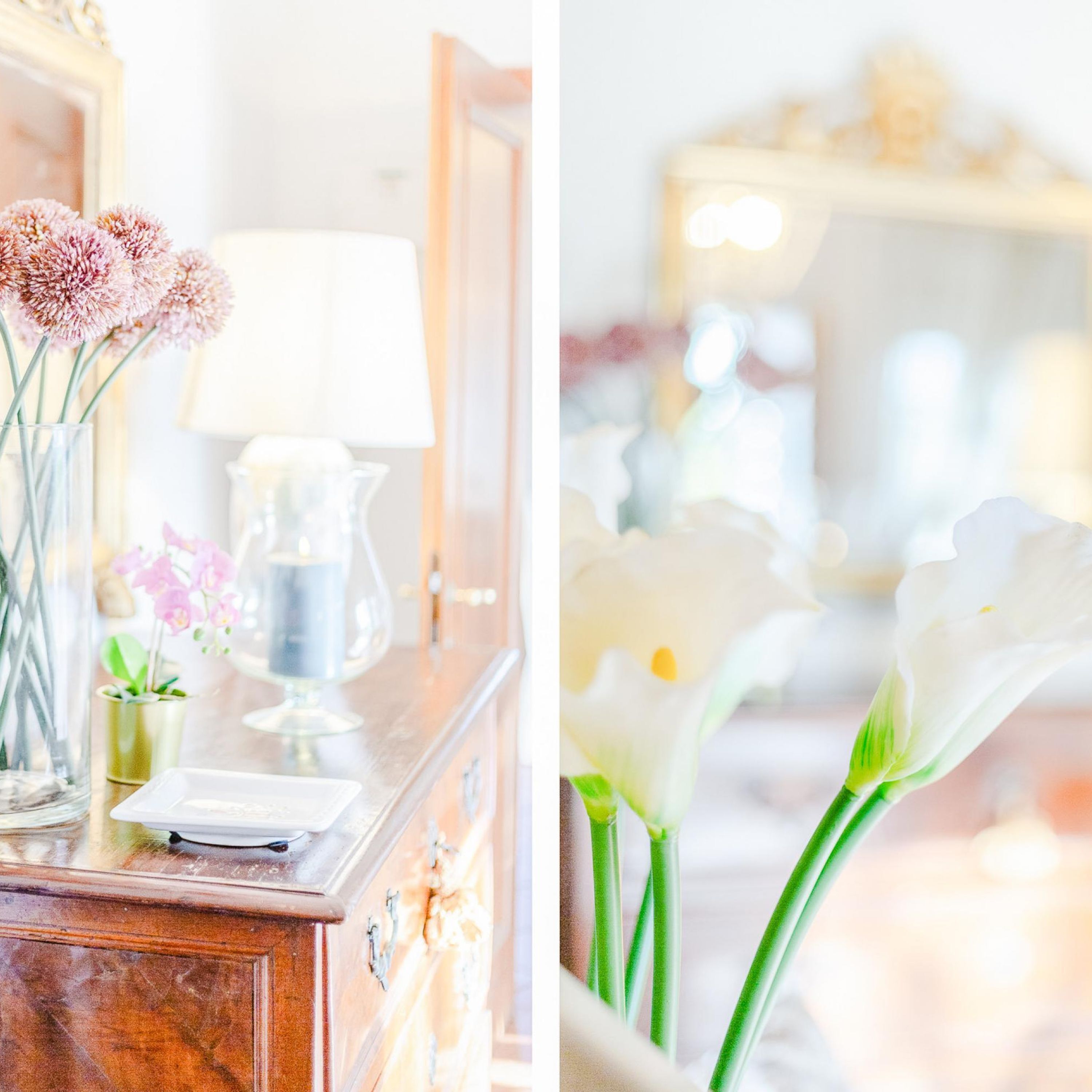 Une commode en bois ornée d’un vase de fleurs roses, d’une lampe et d’une petite plante.