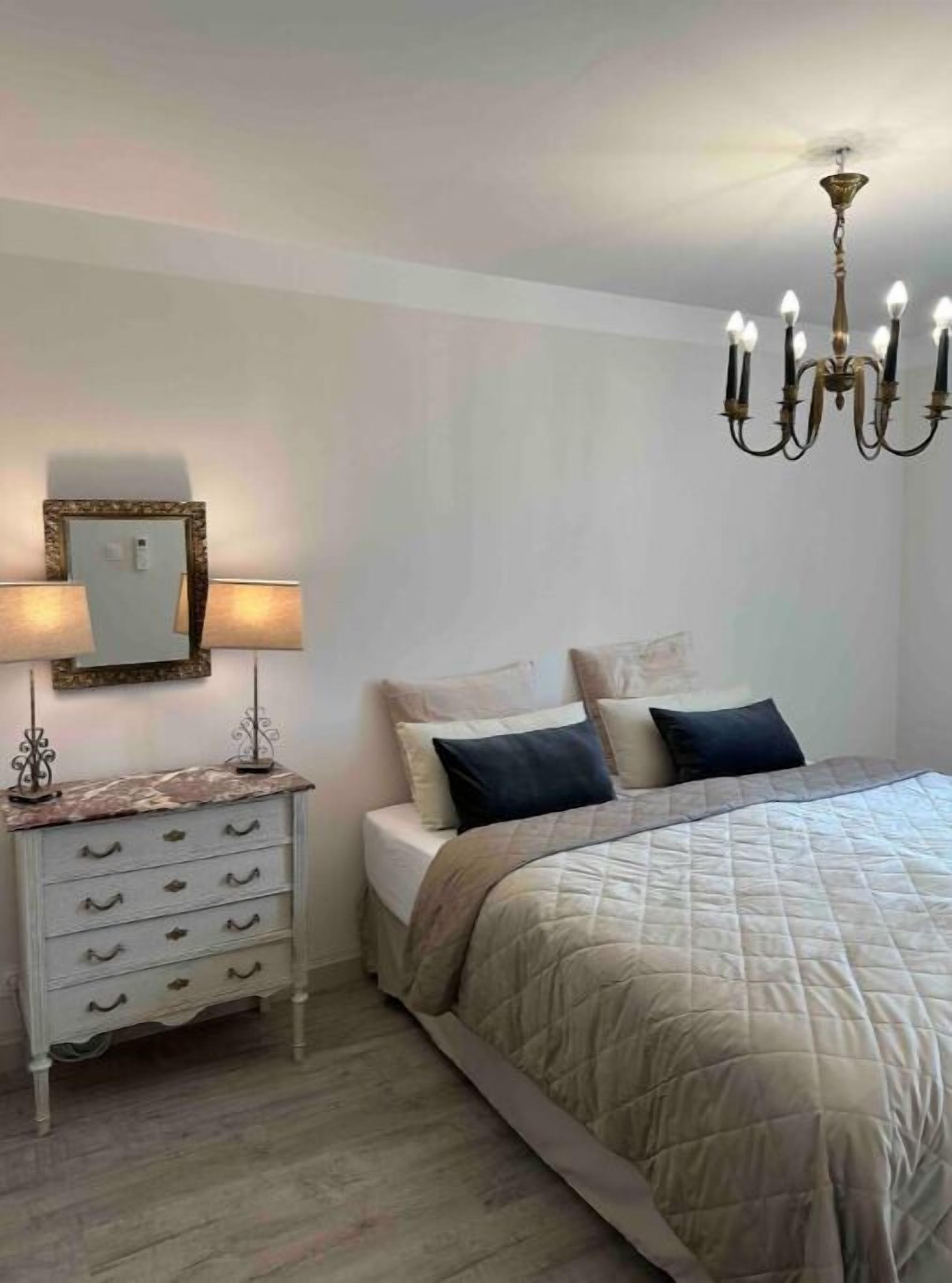 Un dormitorio con cama, cómoda, espejo y candelabro.