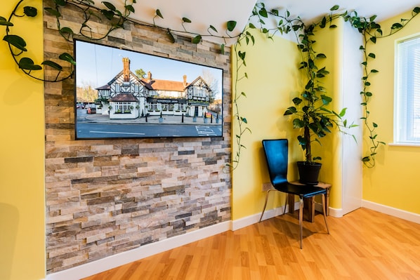 A room with a stone wall, a mounted television displaying a building, a potted plant, and a blue chair.