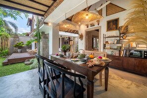 A dining area with a wooden table set for two, surrounded by natural light and featuring woven pendant lights. - Katak Villa by Villa Finder (Ubud)