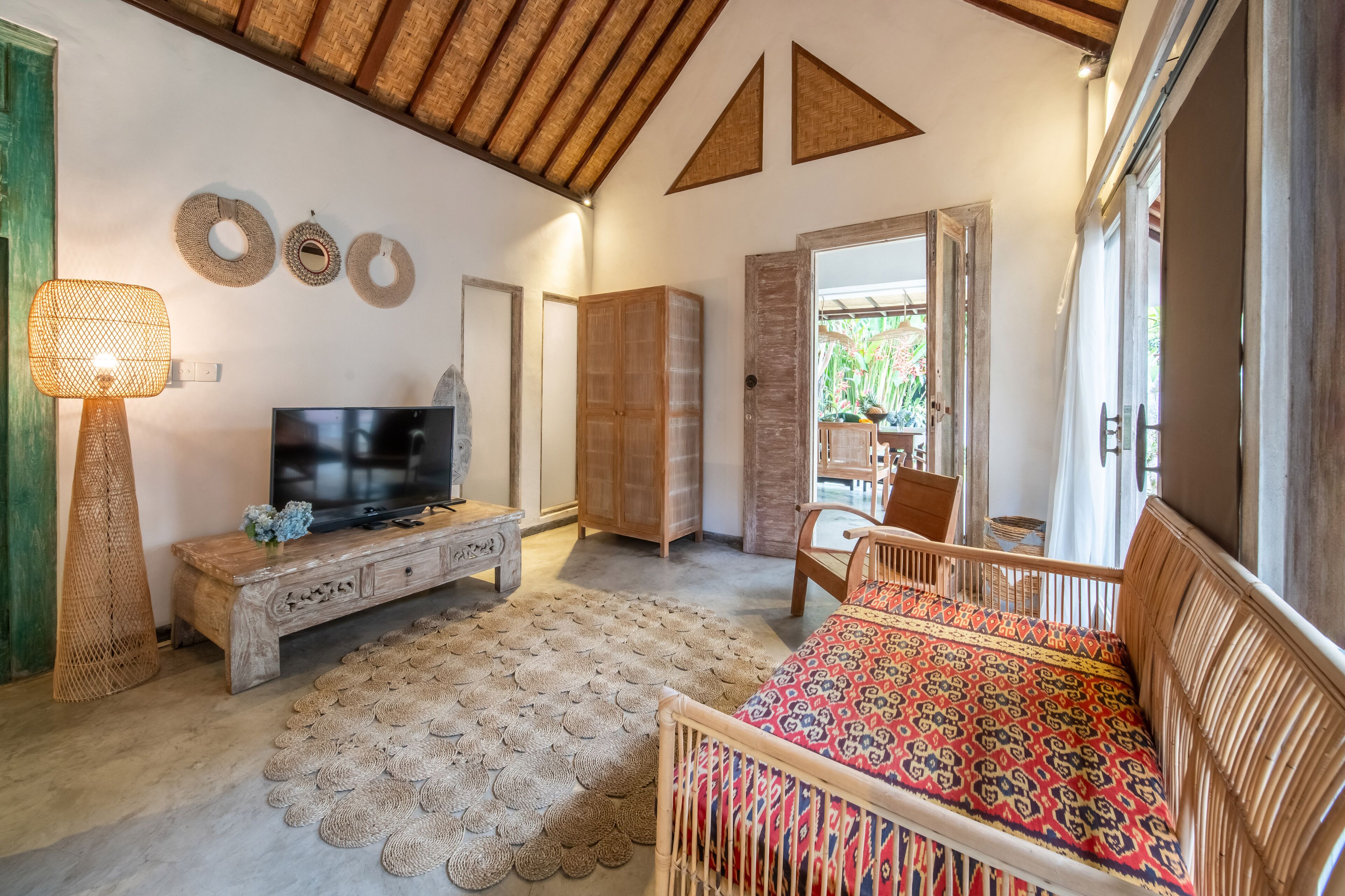 Une pièce chaleureuse avec un plafond en bois, un téléviseur posé sur un meuble en bois, un tapis tissé et un lit recouvert d’une courtepointe à motifs.