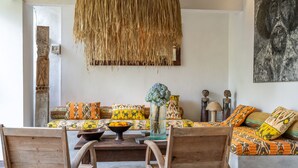 Un salon chaleureux avec un ensemble de canapés, des chaises en bois, un luminaire suspendu en fibres tressées et un vase rempli de fleurs.