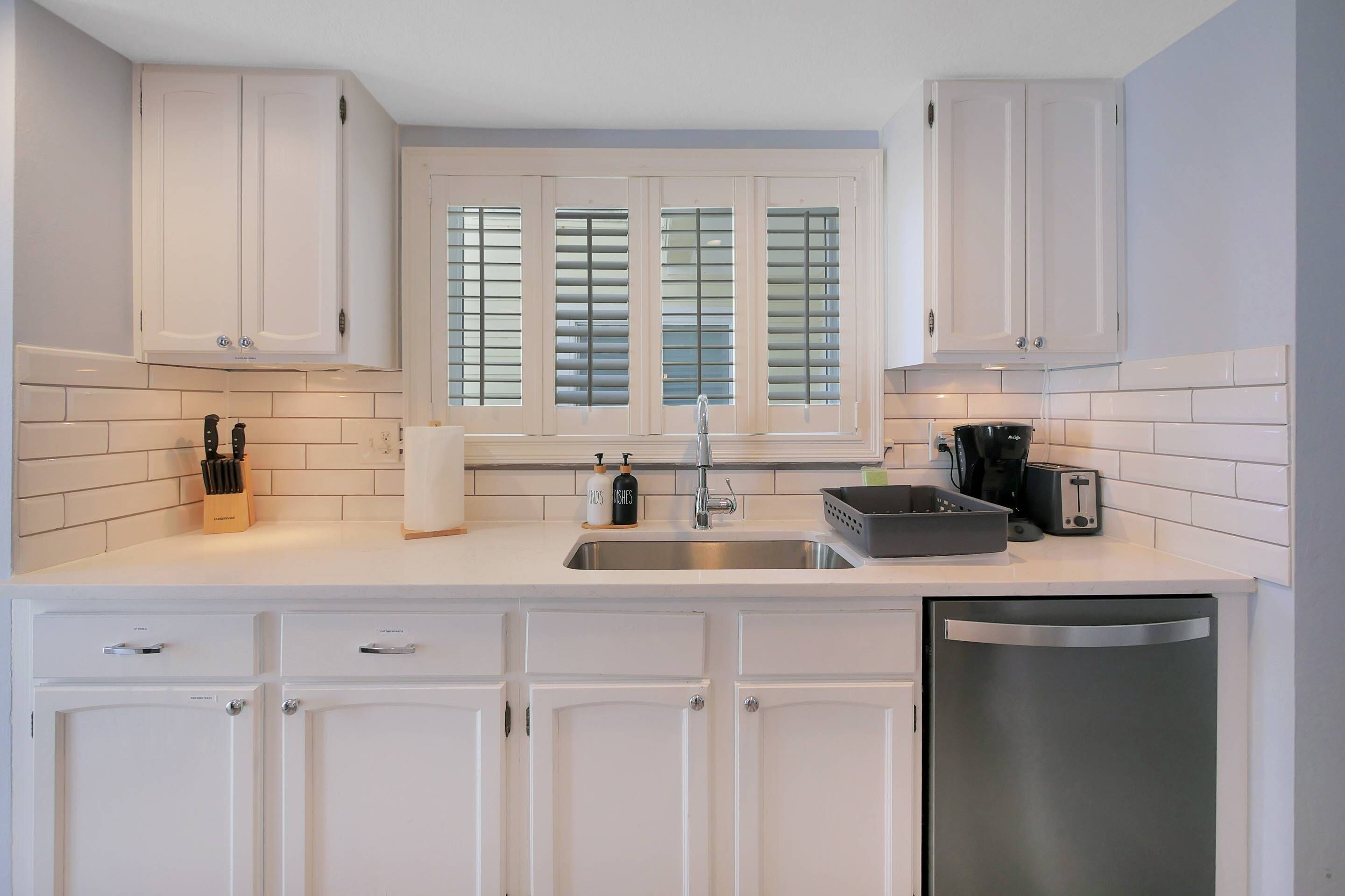 A modern kitchen with white cabinetry, a stainless steel sink, and a dishwasher.