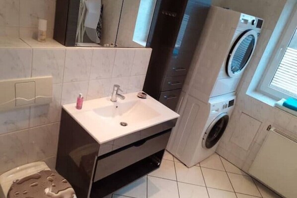 A compact bathroom with a sink, mirror, and a washing machine. - Schöne und Ruhige Ferienwohnung in Ottendorf (Sebnitz)
