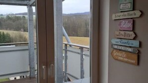 A room with a view of a field and mountains through a glass door. There are signs on the wall with German text. - Schöne und Ruhige Ferienwohnung in Ottendorf (Sebnitz)