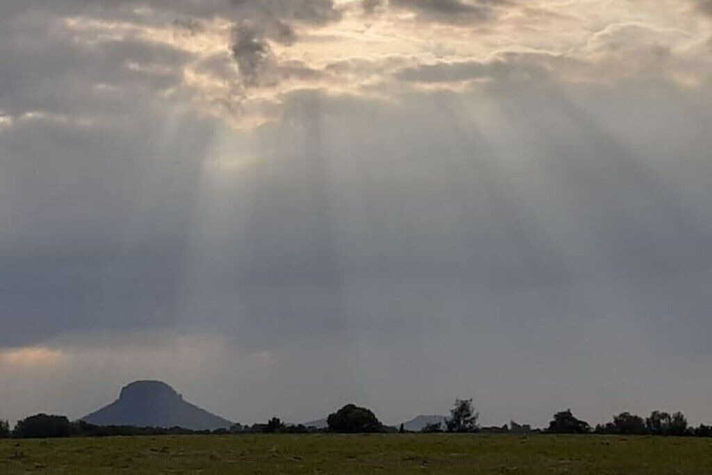 A landscape with a prominent hill or mountain in the distance, a flat field in the foreground, and a cloudy sky.