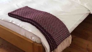 A neatly made bed with a patterned throw, green pillows, and a bedside plant. - The Mountains are Calling Retreat (Quarten)