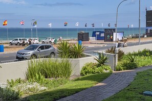 Uma estrada costeira com carros estacionados, um passeio com plantas e bandeiras.