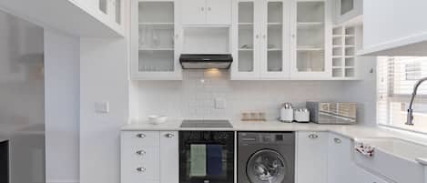 A modern kitchen with white cabinetry, a built-in oven, a dishwasher, and a washing machine.