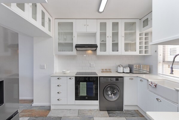 A modern kitchen with white cabinetry, a built-in oven, a dishwasher, and a washing machine.