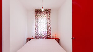 A bedroom with a bed, a nightstand, a lamp, and a door.