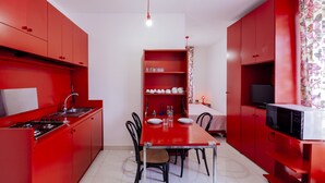 A compact kitchen with red cabinetry, a dining table, chairs, a microwave, and a television.