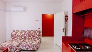 A compact living space with a sofa, a red cabinet, and a kitchen area with a stove.