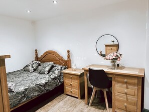 Quarto com cama, escrivaninha de madeira, cadeira, espelho e vaso com flores.