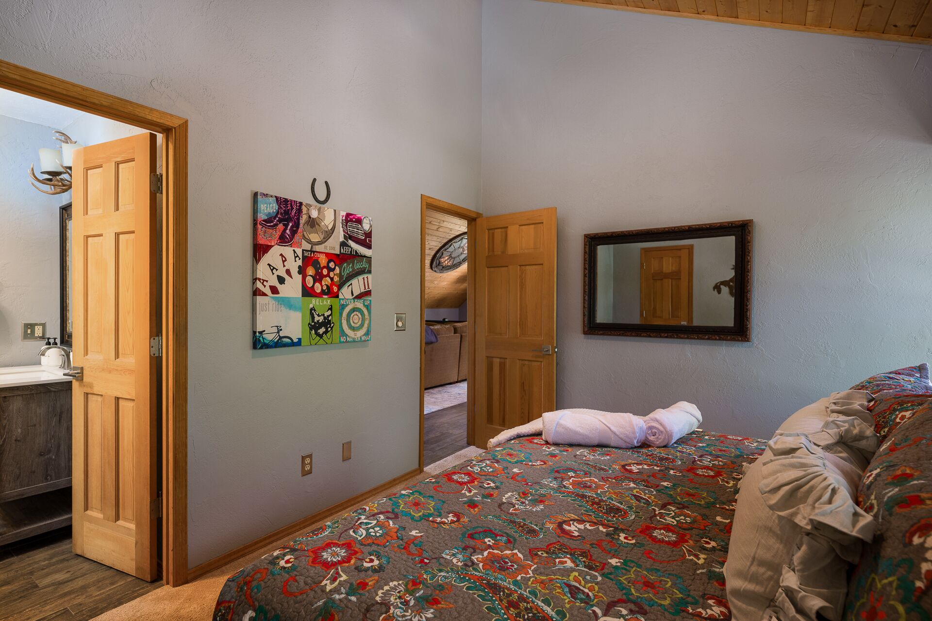 A bedroom with a bed, a wall-mounted mirror, and a door leading to another room.