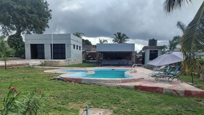 Una piscina con borde de piedra, rodeada de césped y algunas palmeras.