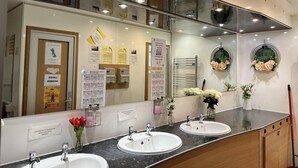 A modern bathroom with two sinks, a large mirror, and various informational posters. - Beautiful Twin Glamping Pod in Salisbury (Salisbury)