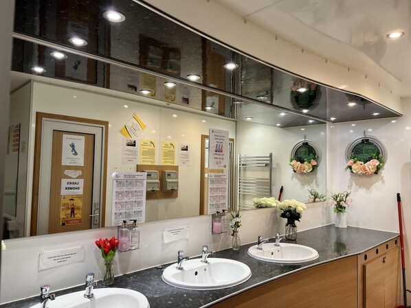 A modern bathroom with two sinks, a large mirror, and various informational posters.