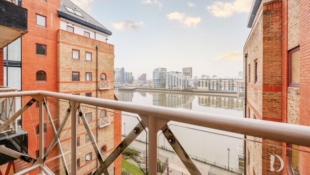 A view from a balcony overlooking a river with modern buildings in the background. - Beautiful 1 Bed on the River (London)